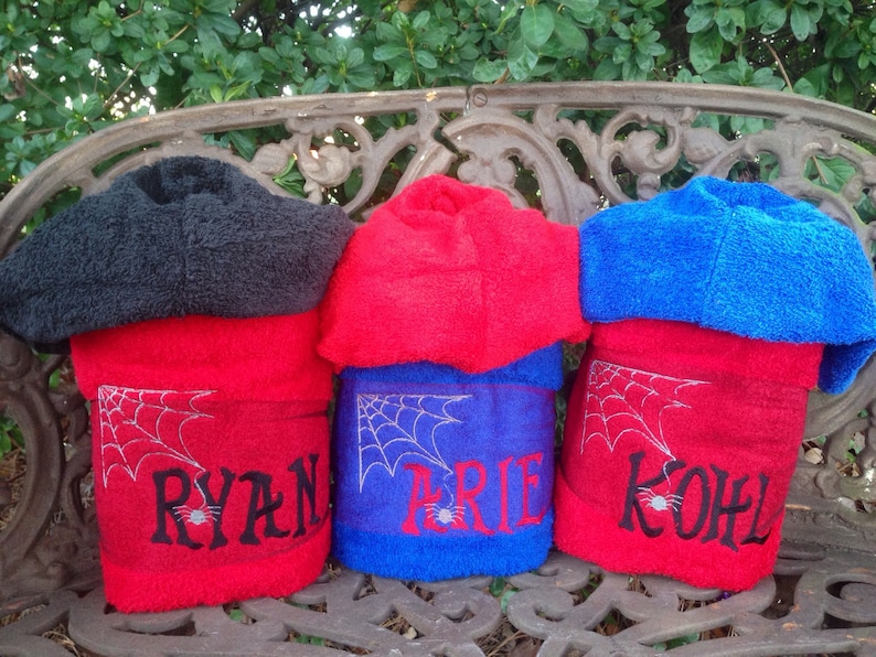 Puede incluir: Tres toallas con capucha con telara&ntilde;as bordadas y nombres: Ryan, Brie y Kohl. Las toallas son rojas, azules y negras.