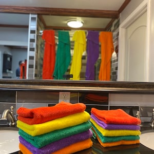 Peut inclure: Une pile de serviettes de bain de couleur arc-en-ciel pli&eacute;es soigneusement sur un comptoir de salle de bain. Les serviettes sont orange, jaune, verte, violette et orange.