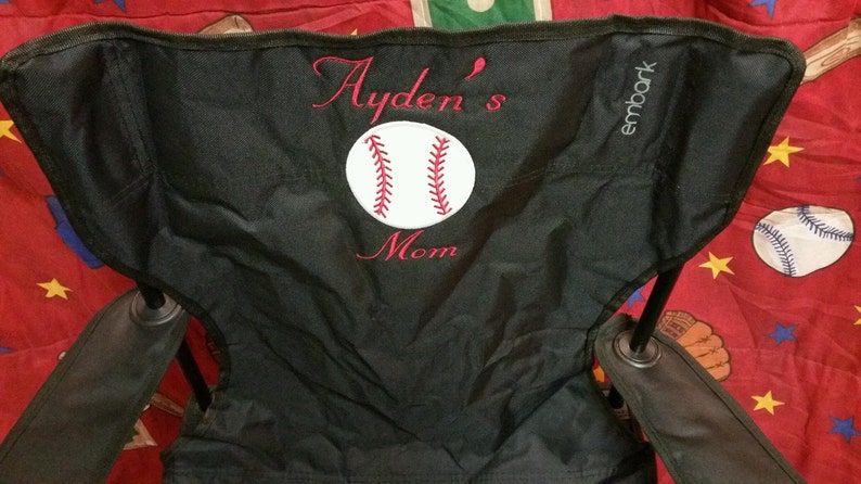 Pu&ograve; includere: Sedia pieghevole nera con una palla da baseball bianca e cuciture rosse ricamate sullo schienale. La sedia ha il testo "Ayden's Mom" e il marchio "embark" ricamato sullo schienale.