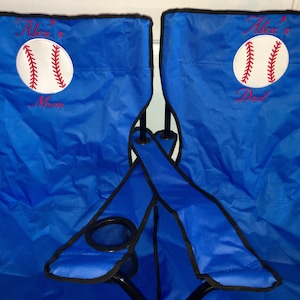Pu&ograve; includere: Due sedie pieghevoli blu con bordi neri e porta bicchieri. Le sedie sono personalizzate con palline da baseball ricamate e il testo "Alex's Mom" e "Alex's Dad".