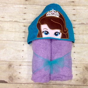 May include: A purple hooded towel with a turquoise hooded top featuring an embroidered princess with a crown. The towel has a turquoise ribbon tied around it.