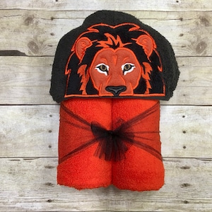 Peut inclure: Serviette &agrave; capuche orange avec un visage de lion noir brod&eacute; sur la capuche. La serviette est nou&eacute;e avec un ruban noir.