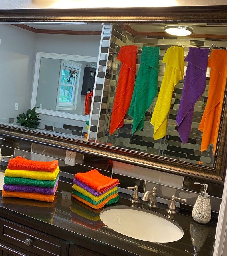 Peut inclure: Une vasque de salle de bain avec un plan de travail en granit noir et un lavabo en porcelaine blanche. Il y a deux piles de serviettes color&eacute;es sur le comptoir et un distributeur de savon liquide. Un miroir au-dessus du lavabo refl&egrave;te une salle de bain avec une douche et plusieurs serviettes color&eacute;es accroch&eacute;es &agrave; un porte-serviettes.