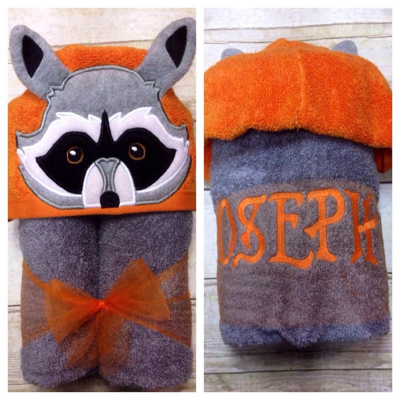 May include: A gray hooded towel with an orange raccoon face on the hood. The towel is tied with an orange ribbon and has the name "JOSEPH" embroidered on the back.