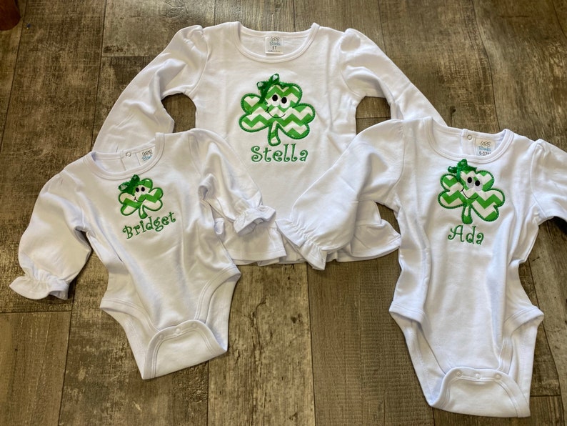 May include: Three white long-sleeved shirts with green shamrock designs and personalized names: Bridget, Stella, and Ada.