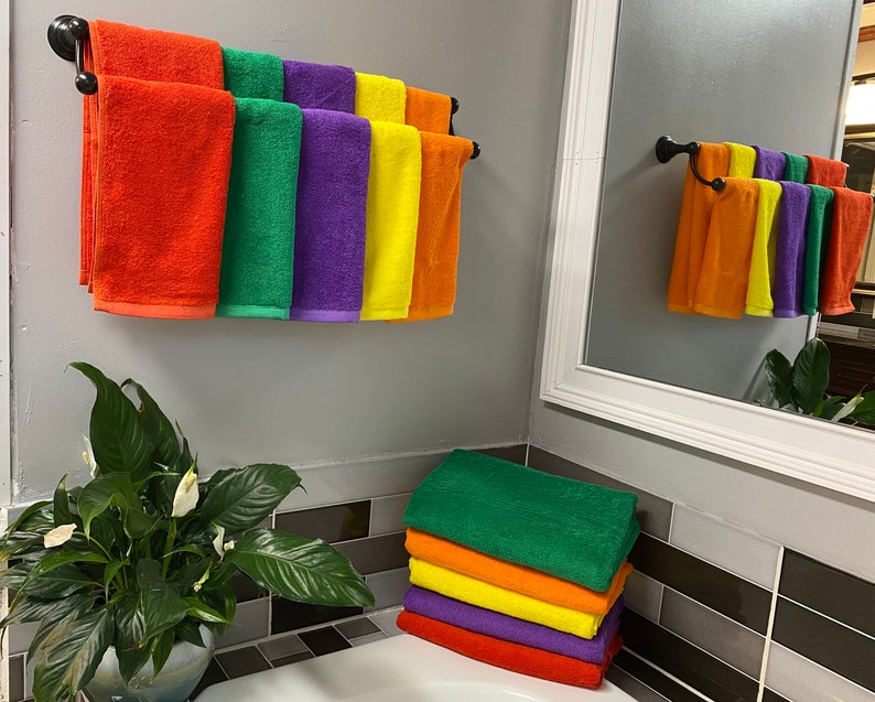 Peut inclure: Une salle de bain avec un porte-serviettes sur lequel sont accroch&eacute;s sept serviettes aux couleurs de l'arc-en-ciel. Les serviettes sont orange, verte, violette, jaune et bleue. Il y a une plante en pot sur le comptoir sous le porte-serviettes.