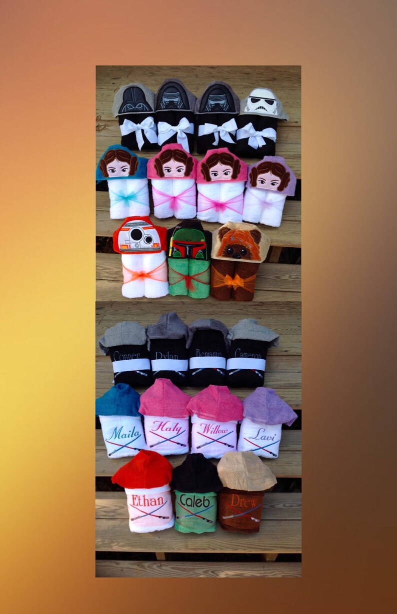 May include: A collection of hooded towels featuring various Star Wars characters embroidered on them. The towels are arranged in rows on a wooden surface. Some towels have names embroidered on them, such as "Connor", "Dylan", "Maile", and "Ethan".