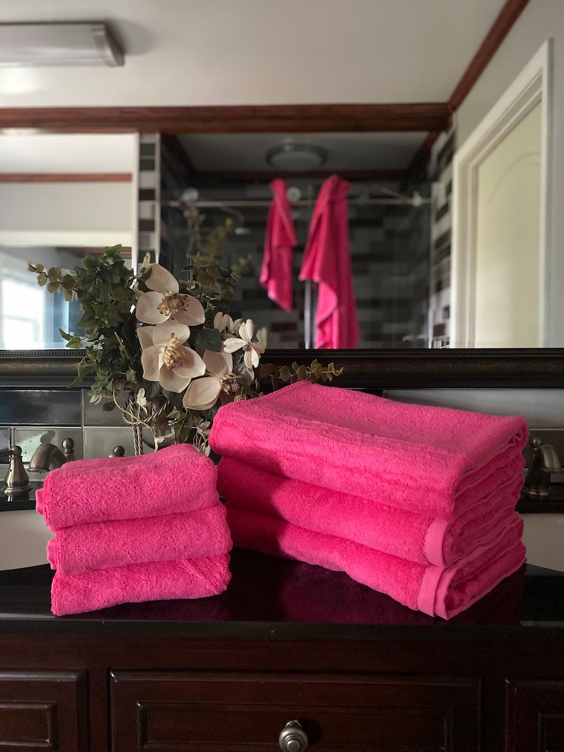 Pu&ograve; includere: Un mucchio di quattro asciugamani da bagno rosa su un piano di lavoro marrone scuro. Gli asciugamani sono morbidi e soffici, e sono perfetti per asciugarsi dopo una doccia o un bagno.