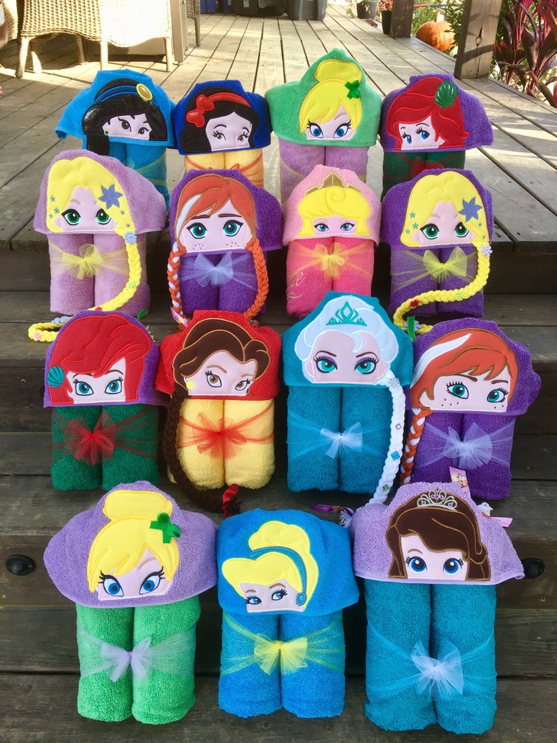May include: A collection of 14 hooded towels featuring different Disney princess characters. Each towel is made of soft, absorbent material and features a colorful embroidered design of a princess's face. The towels are arranged in two rows, with each row containing seven towels.