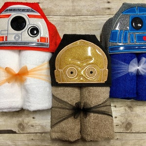 May include: Three hooded towels featuring embroidered Star Wars characters. The towels are rolled up and tied with ribbon. The characters are R2-D2, C-3PO, and BB-8.