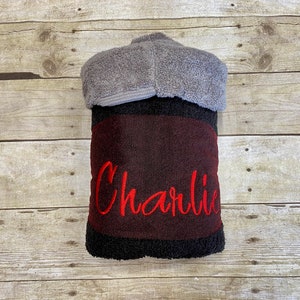 Puede incluir: Una toalla con capucha negra y burdeos con el nombre "Charlie" bordado en rojo.