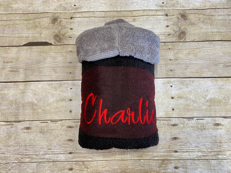 Puede incluir: Una toalla con capucha negra y burdeos con el nombre "Charlie" bordado en rojo.