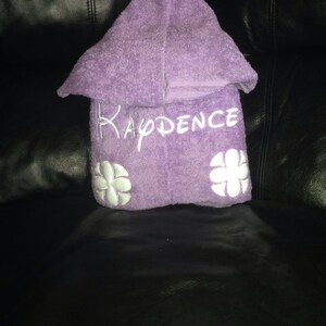 May include: Purple hooded towel with white embroidered flowers and the name "KADENCE" on the front.