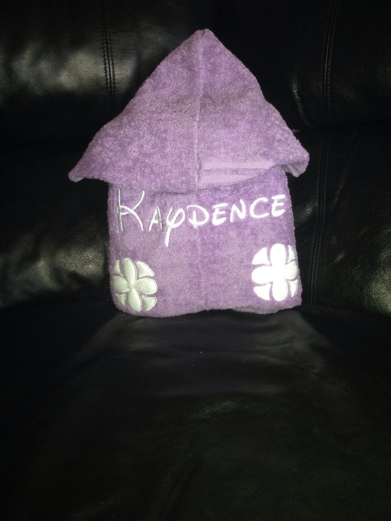 May include: Purple hooded towel with white embroidered flowers and the name "KADENCE" on the front.