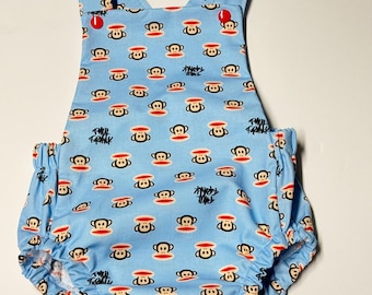 May include: Light blue baby romper with a repeating pattern of cartoon monkeys wearing red and white hats. The romper has a cross-back design and elasticated leg openings. The words "Paul Frank" are printed on the fabric.