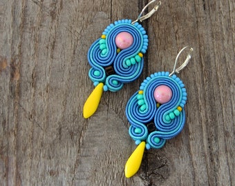May include: A pair of blue, turquoise, and yellow earrings with pink beads. The earrings are made of polymer clay and have a unique, intricate design.
