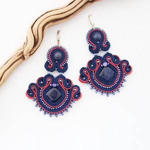 May include: A pair of blue and red earrings with a lapis lazuli stone in the centre of each earring. The earrings are made using a technique called peyote stitch.