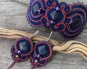 May include: A handcrafted jewelry set featuring a necklace and matching earrings. The set showcases a navy blue and coral design with square, dark blue gemstones. The earrings have a teardrop-shaped dangle. The necklace is connected by a silver chain.
