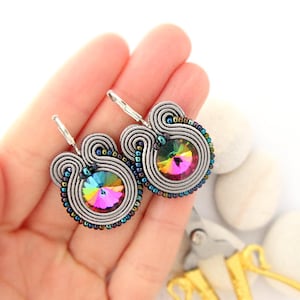May include: A pair of silver earrings with a rainbow iridescent crystal in the center. The earrings are made with silver wire and beads.
