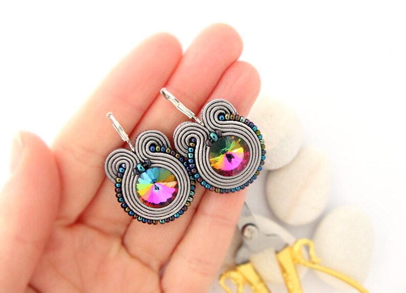 May include: A pair of silver earrings with a rainbow iridescent crystal in the center. The earrings are made with silver wire and beads.