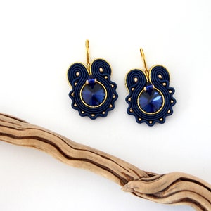 May include: A pair of blue and gold earrings with a dark blue crystal in the center of each earring.