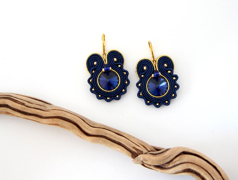 May include: A pair of blue and gold earrings with a dark blue crystal in the center of each earring.