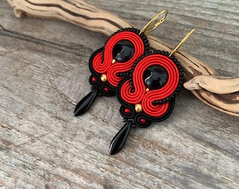 May include: A pair of red and black dangle earrings with black teardrop-shaped accents. The earrings are made with a woven thread technique and feature black beads.