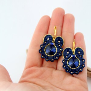 May include: A pair of blue and gold earrings with a dark blue crystal in the center of each earring.
