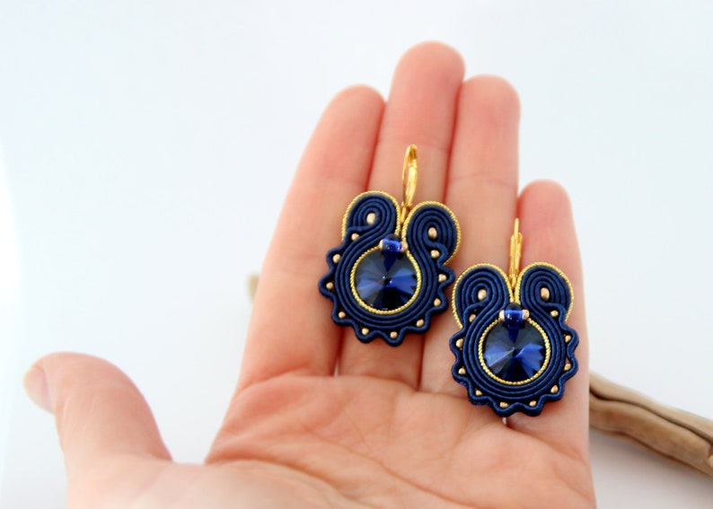 May include: A pair of blue and gold earrings with a dark blue crystal in the center of each earring.