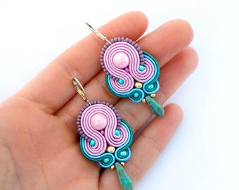 May include: A pair of pink, green, and gold earrings with a pearl accent. The earrings are made of crocheted thread and have a turquoise stone dangle.