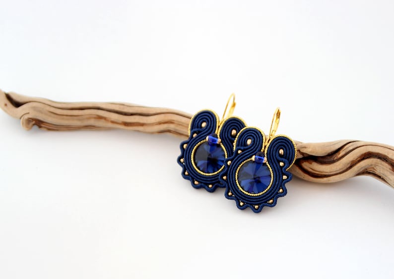 May include: A pair of blue and gold earrings with a dark blue crystal in the center of each earring.