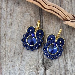 May include: A pair of blue and gold earrings with a round, blue crystal in the center of each earring.