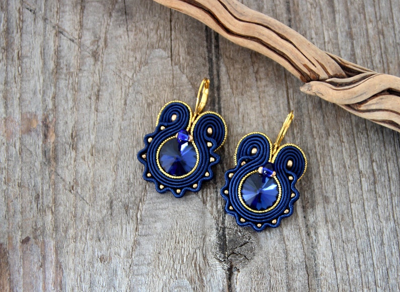 May include: A pair of blue and gold earrings with a round, blue crystal in the center of each earring.