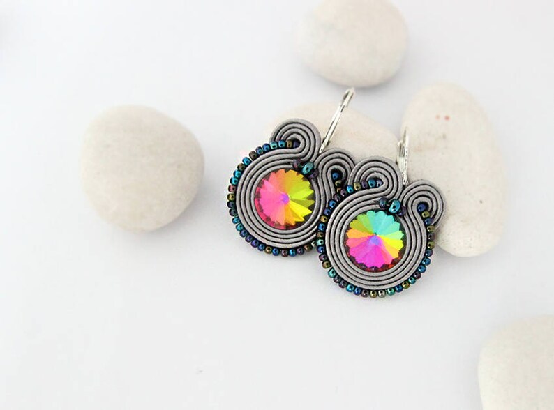 May include: A pair of silver earrings with a rainbow iridescent crystal in the center of each earring. The earrings are made of wire wrapped around a crystal.