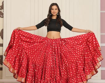 May include: A vibrant red skirt with a gold polka dot pattern and tiered ruffles. The skirt has a gold border at the hem. The model is wearing a black crop top. The skirt is a festive garment.