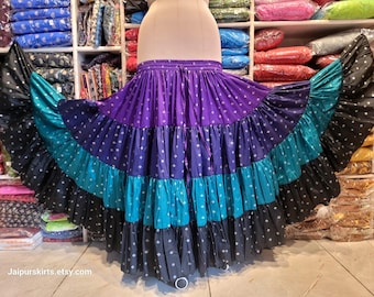 May include: A tiered maxi skirt featuring a purple waistband and upper section, a teal middle tier, and a black bottom tier. The fabric is decorated with a small white geometric pattern throughout. The skirt includes a drawstring waist tie.