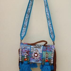 Puede incluir: Un bolso bandolera de patchwork azul y marr&oacute;n con flecos y borlas. El bolso est&aacute; decorado con conchas y cuentas.