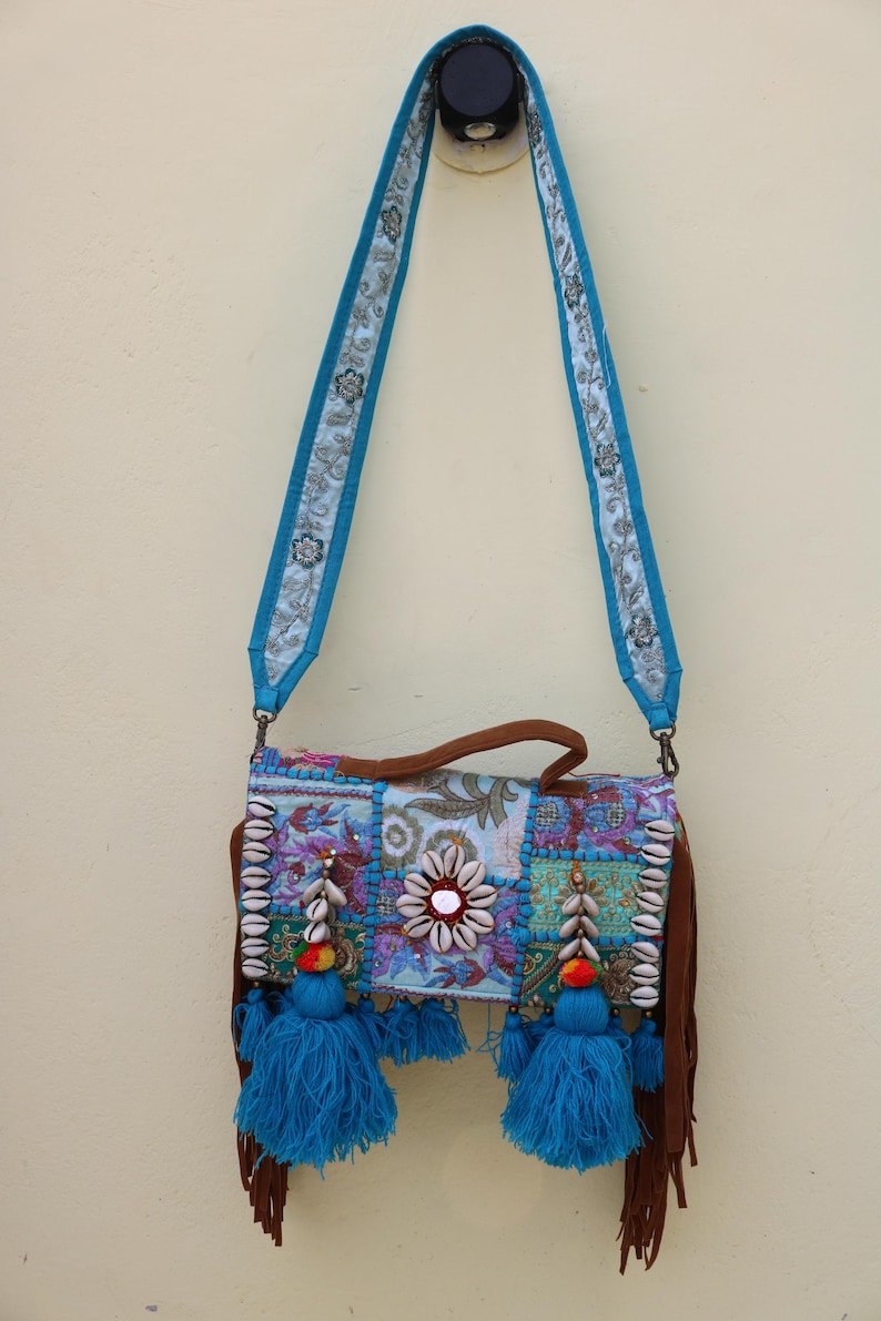 Puede incluir: Un bolso bandolera de patchwork azul y marr&oacute;n con flecos y borlas. El bolso est&aacute; decorado con conchas y cuentas.