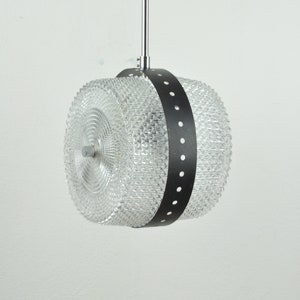 May include: A clear glass pendant light fixture with a black band and silver accents. The glass is textured and has a geometric pattern.