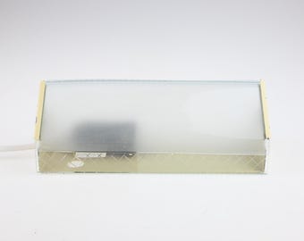 May include: A rectangular wall lamp featuring a frosted glass shade with a subtle diamond-patterned base. The fixture is framed by metallic gold-toned side panels and includes a white electrical cord extending from the left side.