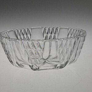 May include: A clear glass bowl with a decorative, diamond-shaped pattern. The bowl is round and has a wide, shallow base.