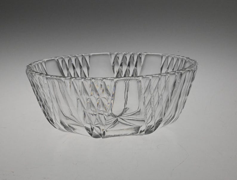 May include: A clear glass bowl with a decorative, diamond-shaped pattern. The bowl is round and has a wide, shallow base.