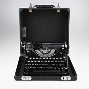 May include: A vintage black Underwood typewriter with a silver carriage and keys, displayed inside its open black carrying case. The typewriter has a classic design with a round key shape and a prominent carriage return lever.
