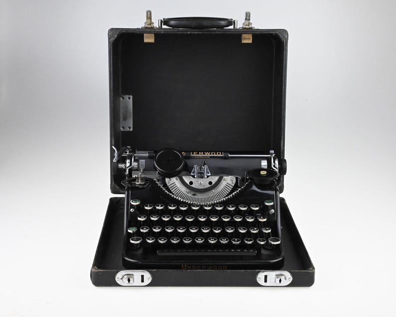 May include: A vintage black Underwood typewriter with a silver carriage and keys, displayed inside its open black carrying case. The typewriter has a classic design with a round key shape and a prominent carriage return lever.