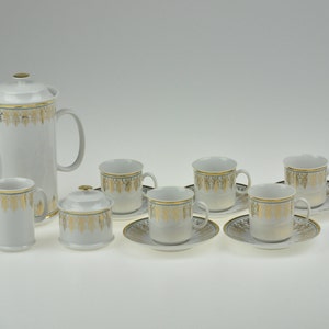 May include: A white porcelain tea set with gold trim. The set includes a teapot, creamer, sugar bowl, and six cups and saucers.