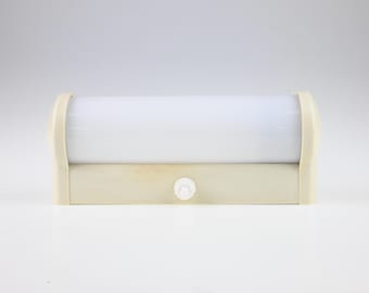 May include: A horizontal wall-mounted light fixture featuring a cylindrical white frosted glass shade supported by a cream-colored plastic base. A small white circular push-button switch is centered on the front of the base.