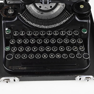 May include: A black Underwood Model X10 typewriter with a QWERTY keyboard layout. The typewriter has round, white keys with black lettering and a silver carriage. The machine sits in a black case with silver latches.