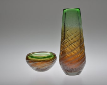 May include: A set of two glass vases with a swirling, textured design. The larger vase is green at the top and fades to orange at the bottom. The smaller vase is a similar design but is smaller and more rounded.