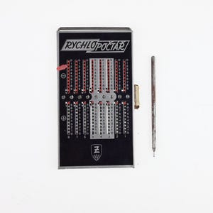 Puede incluir: Una calculadora Rychlopoctar vintage con un marco negro y plateado, con indicadores de números rojos y blancos. Un lápiz óptico de metal y un pequeño trozo de papel están junto a la calculadora sobre un fondo blanco. La calculadora tiene la letra "Z" en la parte inferior.