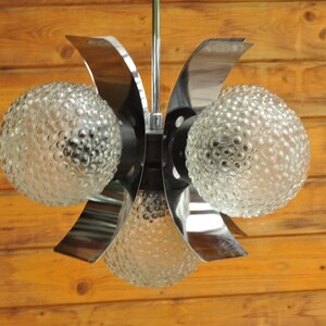 May include: A chrome and glass mid-century modern chandelier with four light bulbs. The glass globes have a textured bubbled surface.
